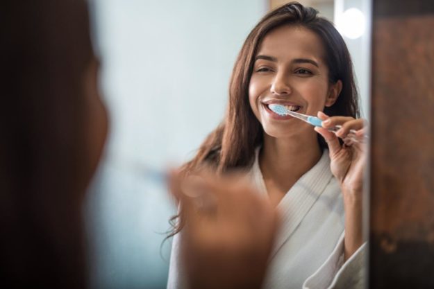 6 Healthy Dental Habits to Protect Your Natural Teeth woman brushing her teeth and practicing health dental habits