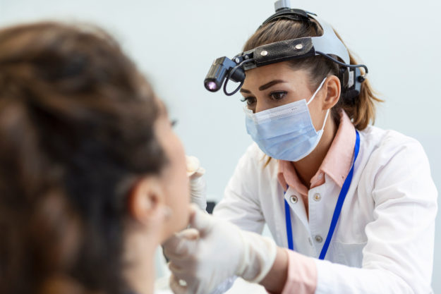 Female patient opening her mouth for the doctor to look in her throat. Otolaryngologist examines sore throat of patient. endodontist helping patient understand loose adult teeth
