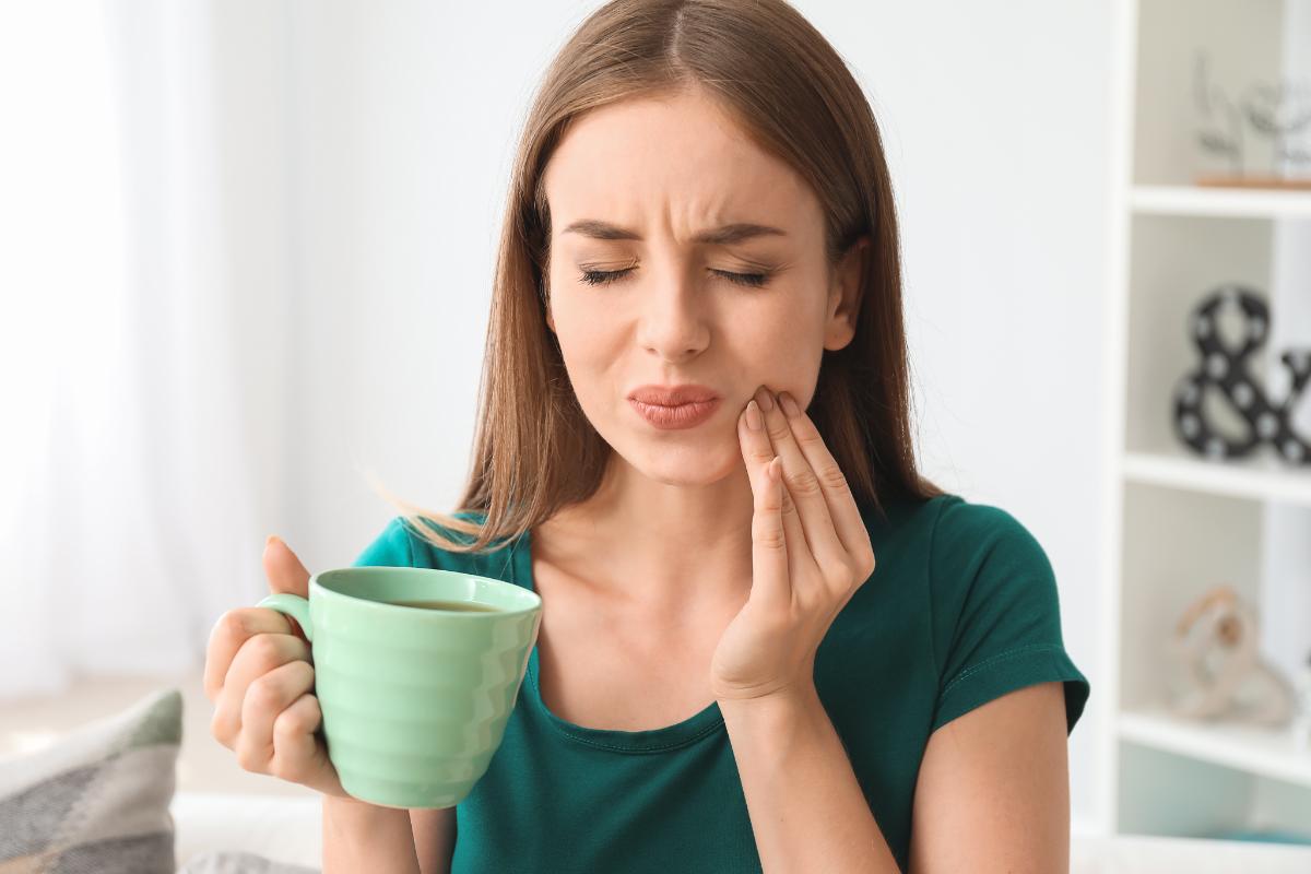 5 Signs That You Need a Root Canal woman holding mug experiences symptoms that she needs a root canal