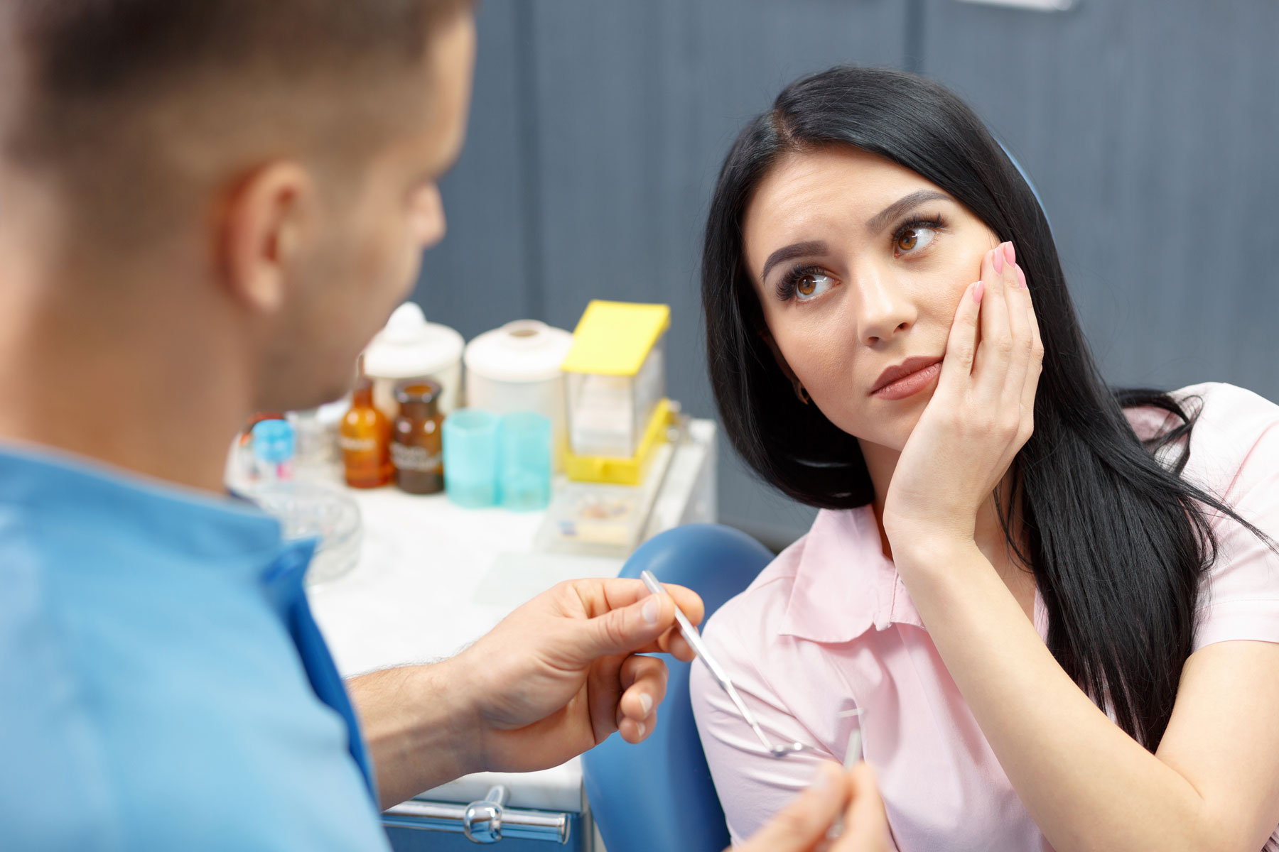3 Common Signs You Need A Root Canal a person holds their jaw while a dentist talks about the signs you need a root canal